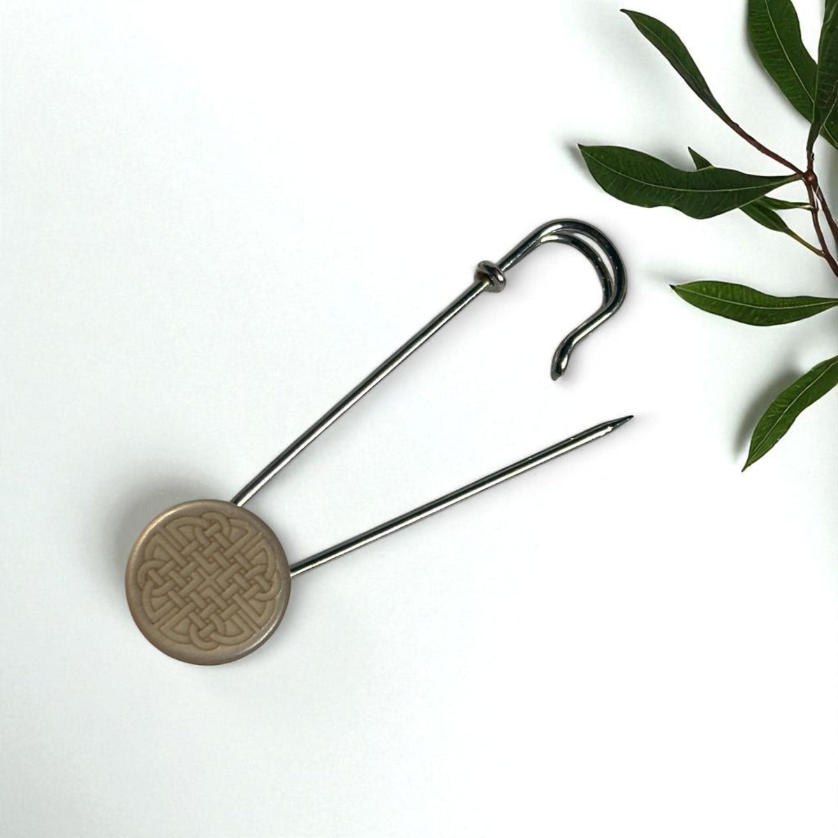 Geöffnete Ponchonadel mit keltischem Knoten vor grünen Blättern