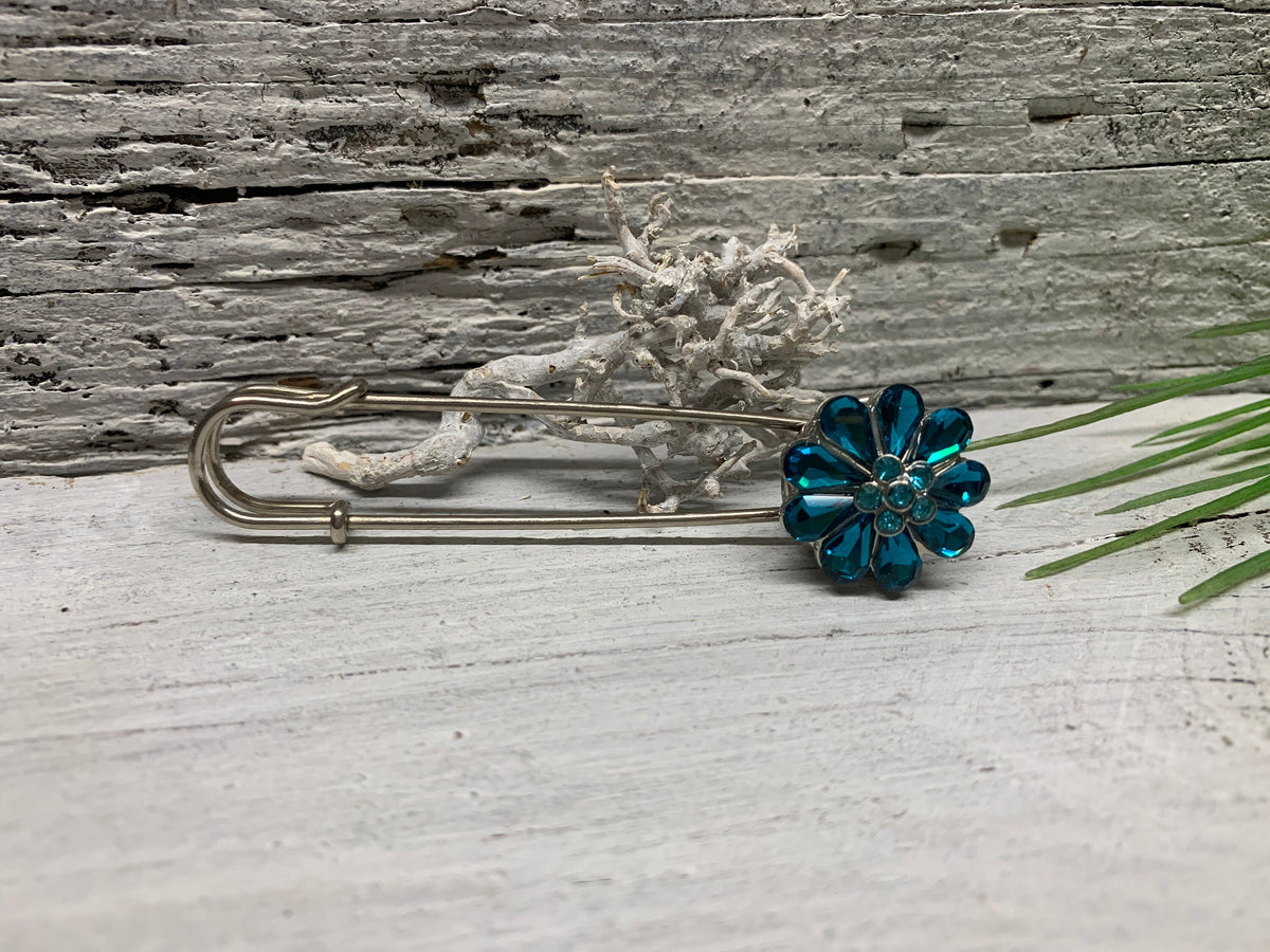 Kiltnadel mit türkisblauer Strass-Blume als Druckknopf auf verwittertem Holz