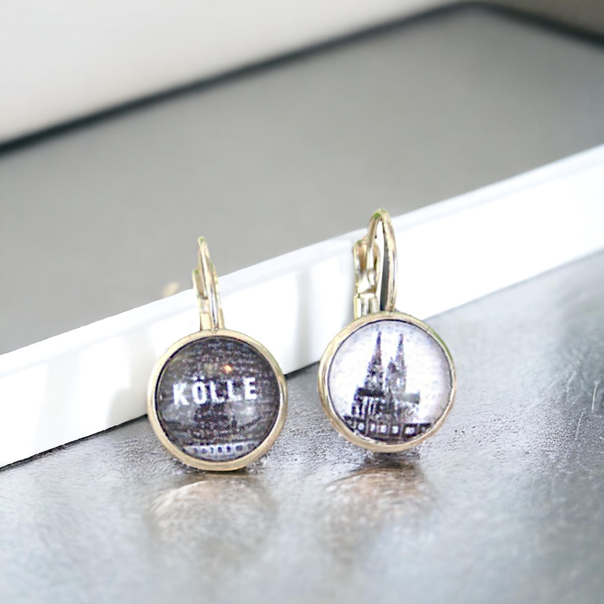 Ohrhänger mit Brisur, ein Motiv mit Schriftzug Kölle, eines mit Kölner Dom, auf hellem Untergrund