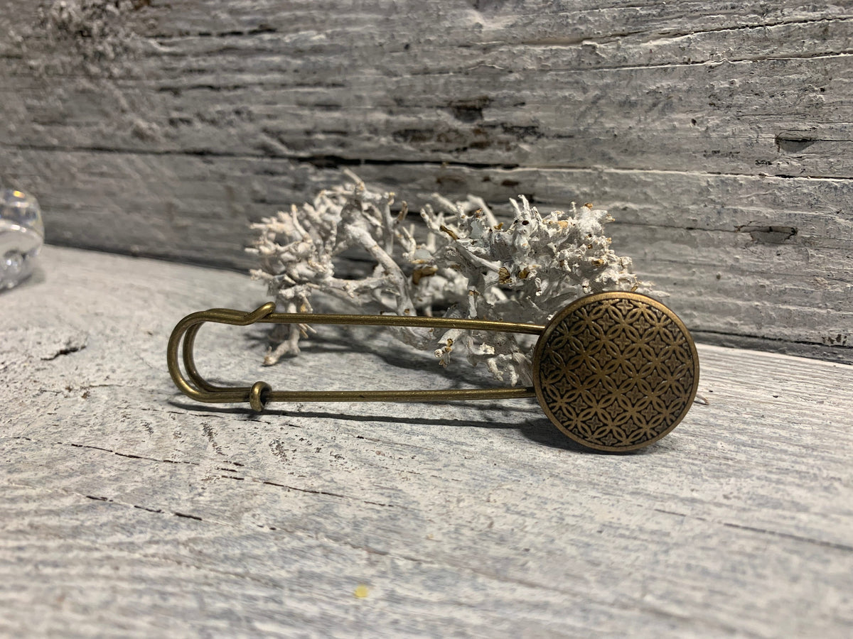 Bronzefarbene Ponchonadel mit Blume des Lebens auf verwittertem Holz vor Trockenflechte