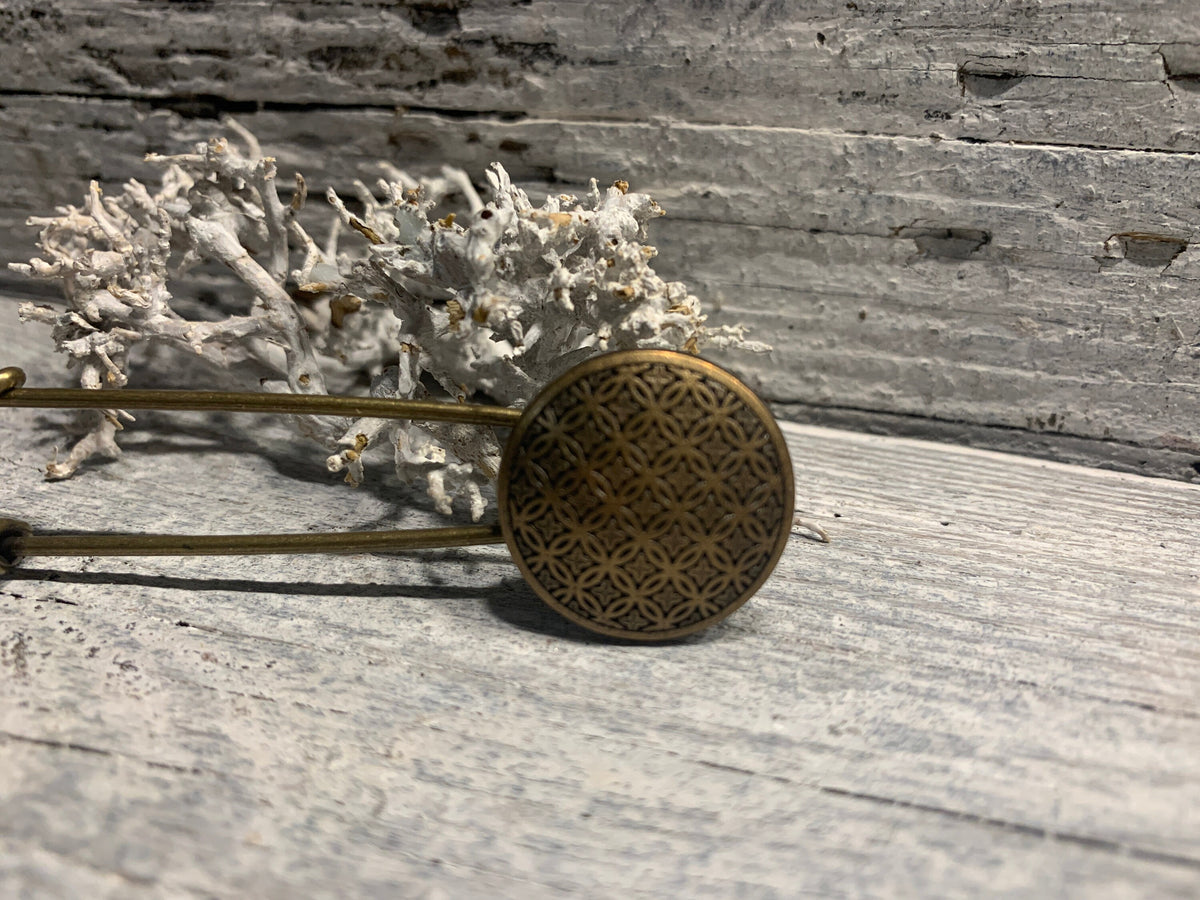 Ponchonadel mit rundem Bronzeelement liegend vor Trockenflechte