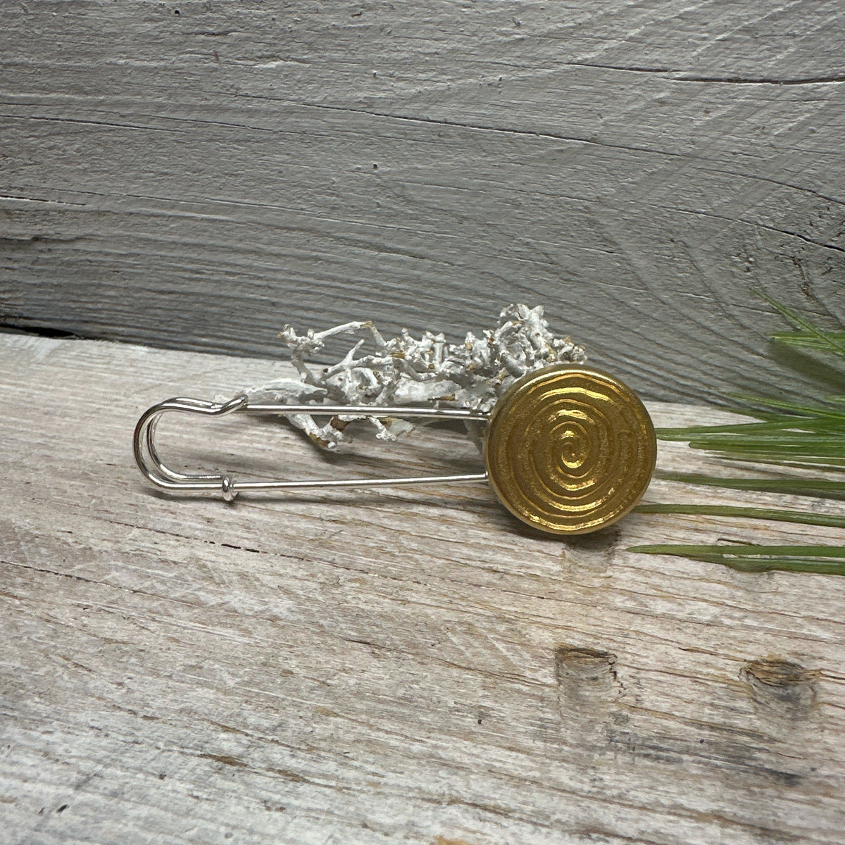 Ponchonadel mit goldfarbener Spirale liegend auf grauem Holz