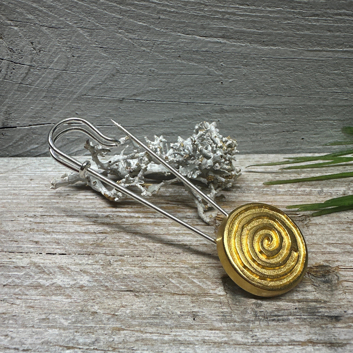 Goldfarbene Spirale in Nahansicht mit silberfarbener Nadel