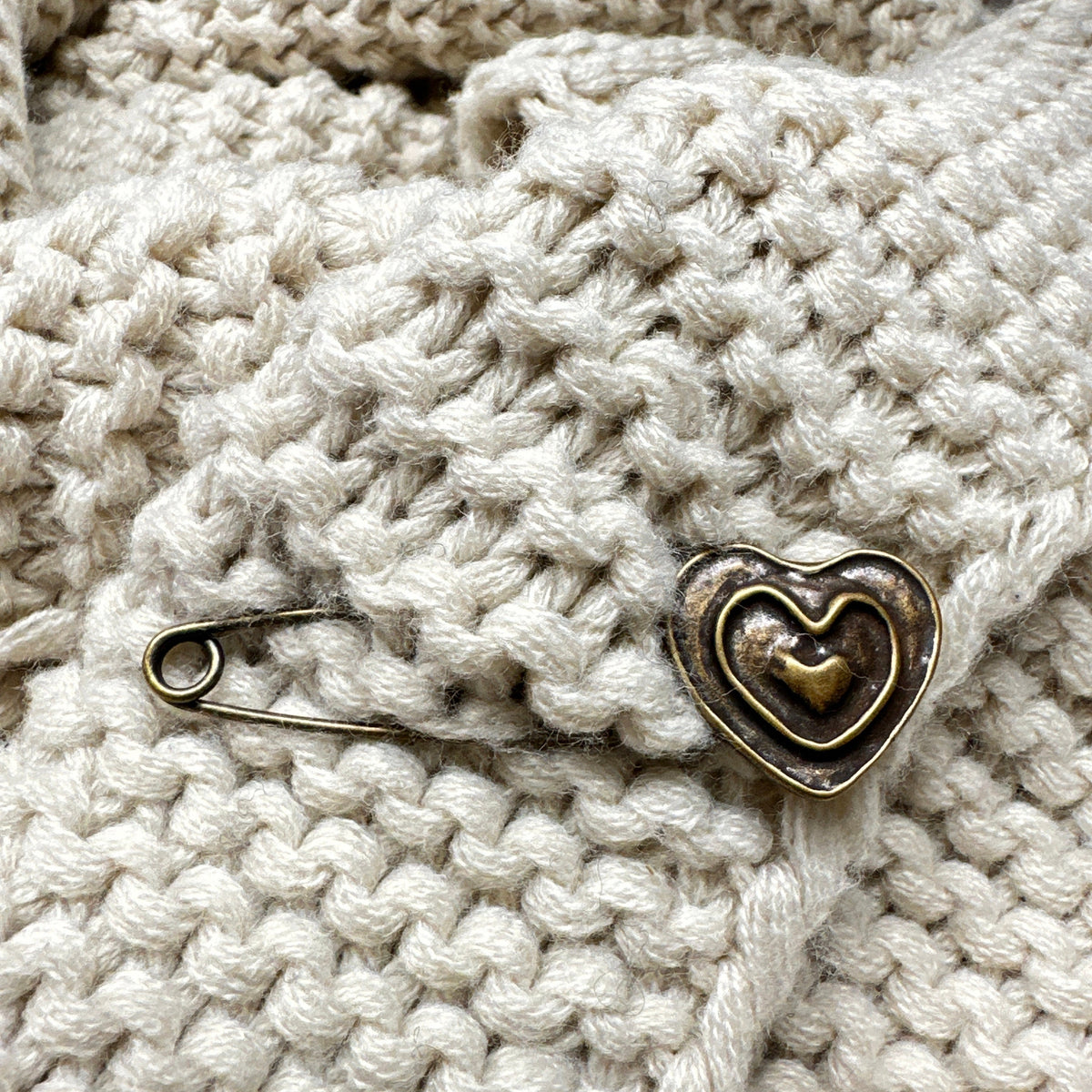 Ponchonadel mit Herz verschließt eine helle Strickjacke