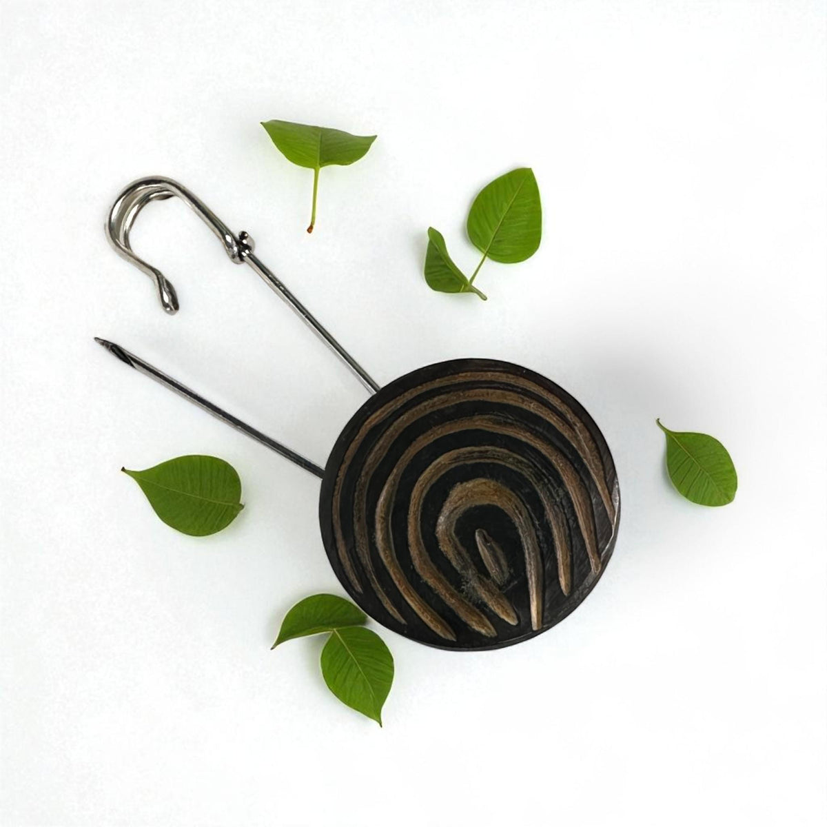 Geöffnete Ponchonadel mit Holz-Spirale neben grünen Blättern