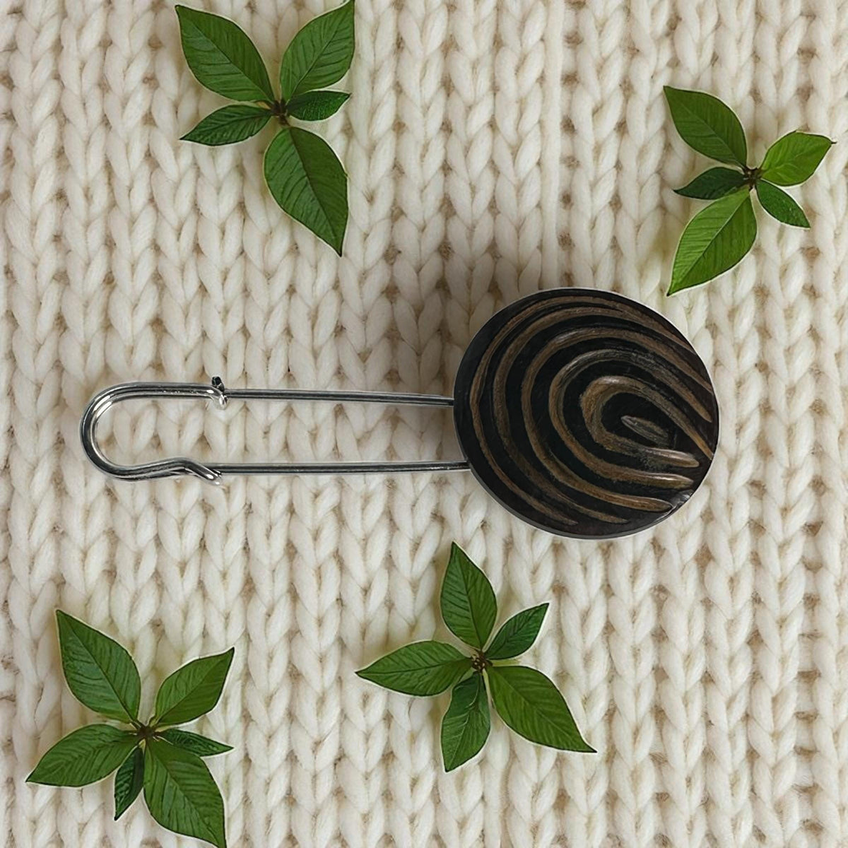 Ponchonadel mit Holz-Spirale auf hellem Strick mit Blättern