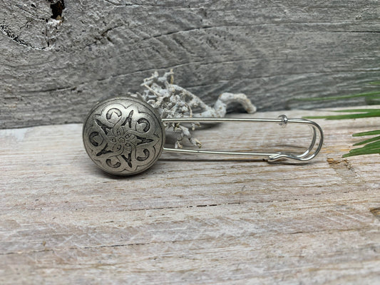 Ponchonadel mit keltischem Blumenstern in Altsilber-Optik auf grauem Holz vor Trockenflechte