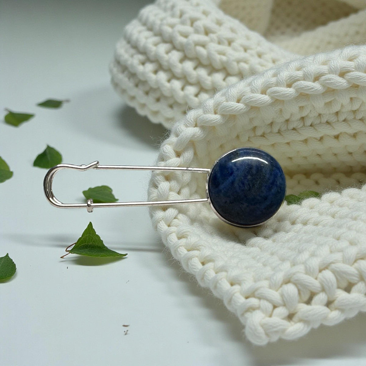 Ponchonadel silberfarben mit rundem Lapis Lazuli an cremeweißem Strickschal mit grünen Zweigen