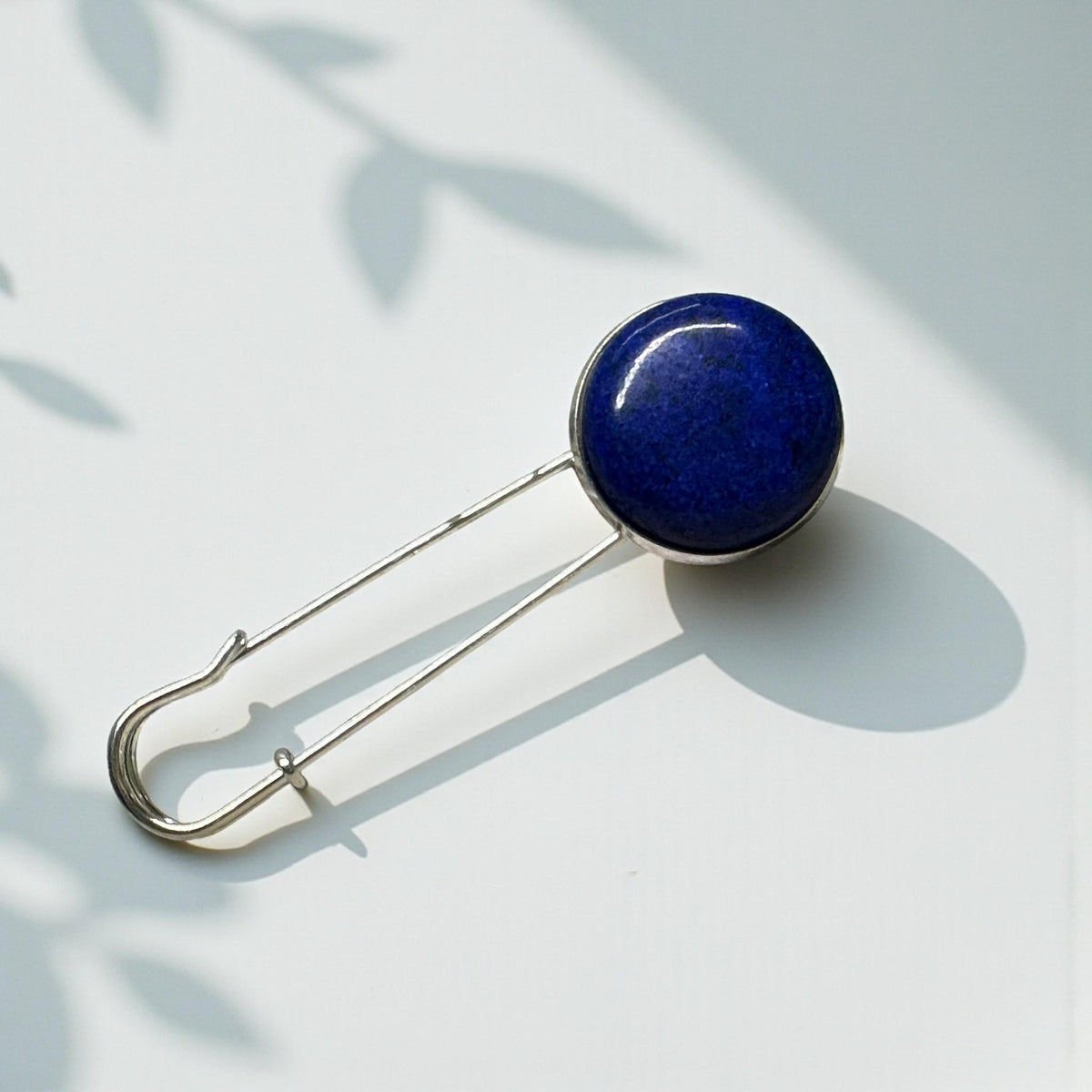 Ponchonadel mit Lapis Lazuli in Königsblau auf weißem Untergrund mit Blattschatten