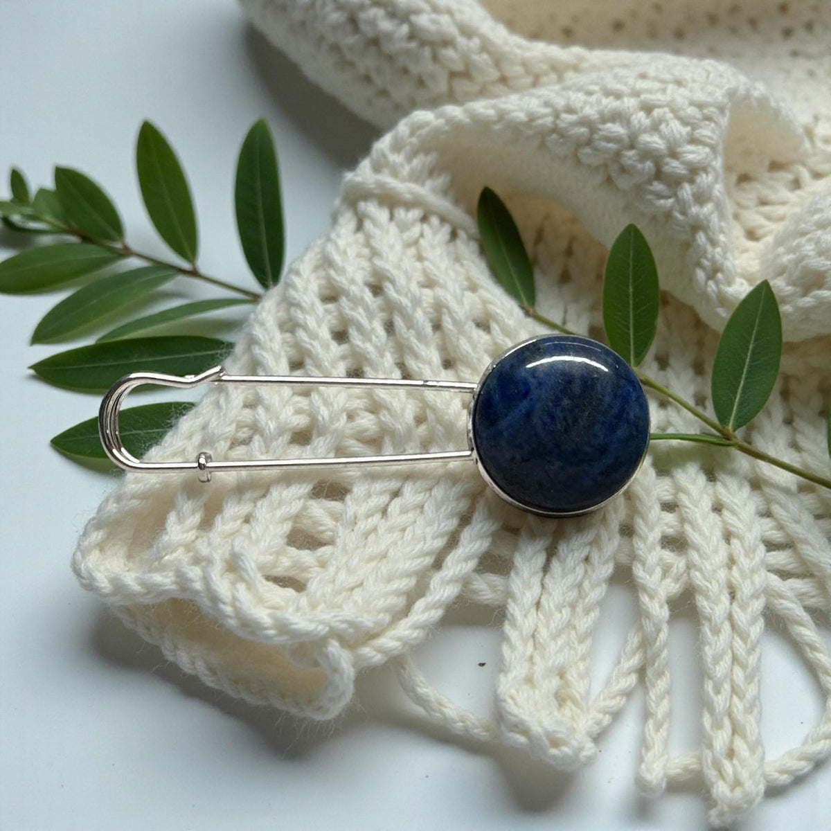 Ponchonadel mit Lapis Lazuli an cremefarbenem Lochmuster-Strick mit grünen Blättern