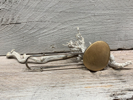 Ponchonadel mit ovalem Element in matter Goldoptik auf verwittertem Holz vor Trockenflechte