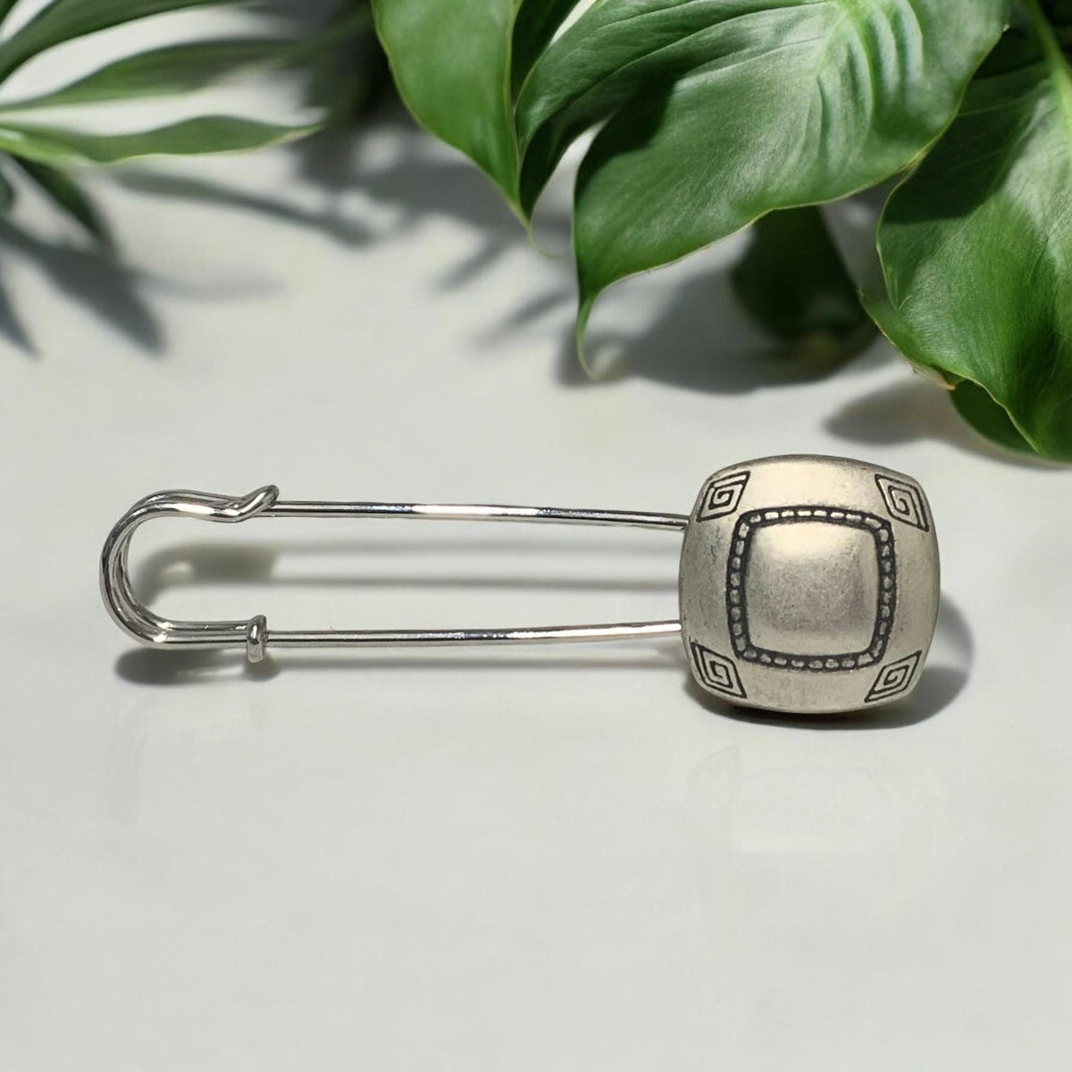 Ponchonadel mit quadratischem Element in Altsilber-Optik vor grünen Blättern