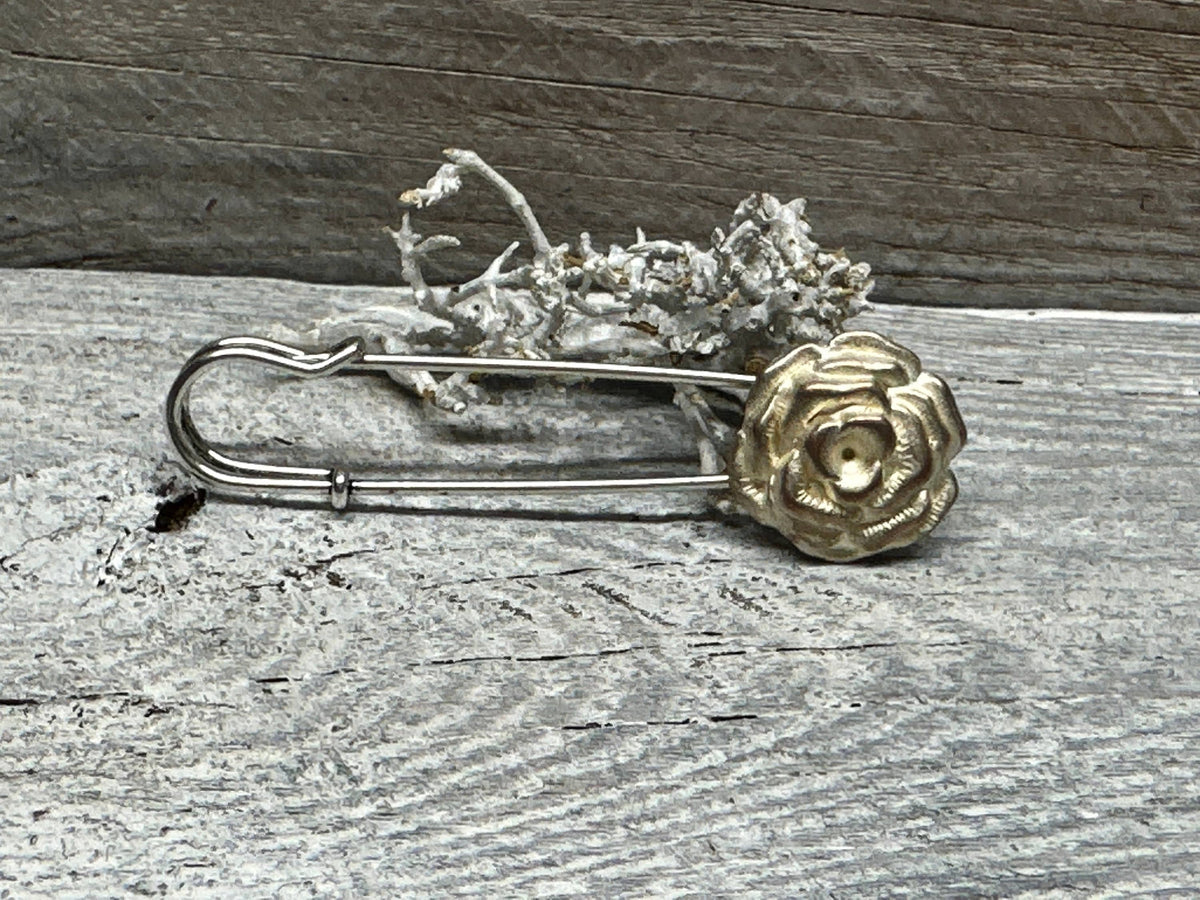 Ponchonadel mit Rosenmotiv in Gold- und Silbertönen auf verwittertem Holz vor Trockenflechte