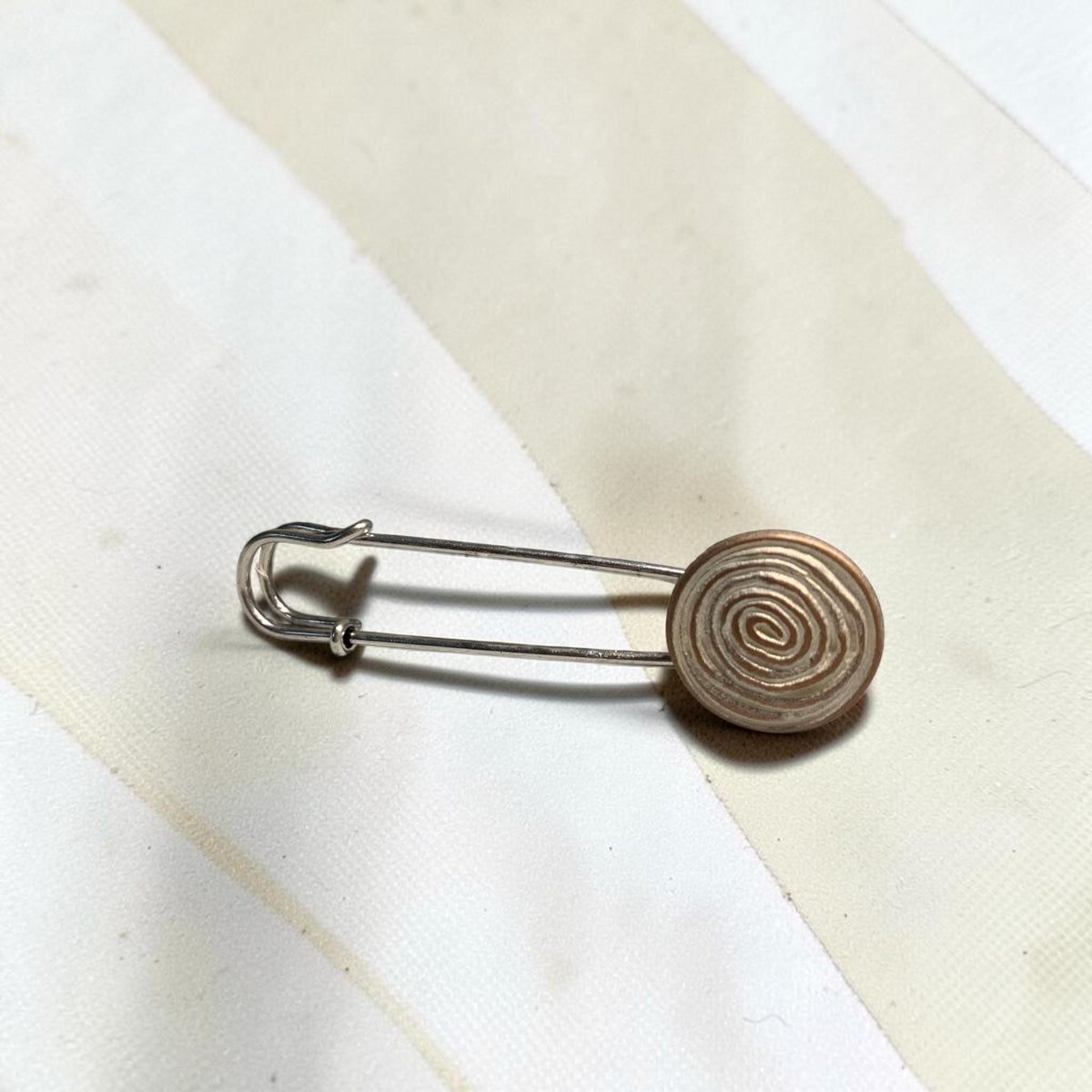 Ponchonadel mit Spiralmotiv in Seitenansicht auf hellem Grund