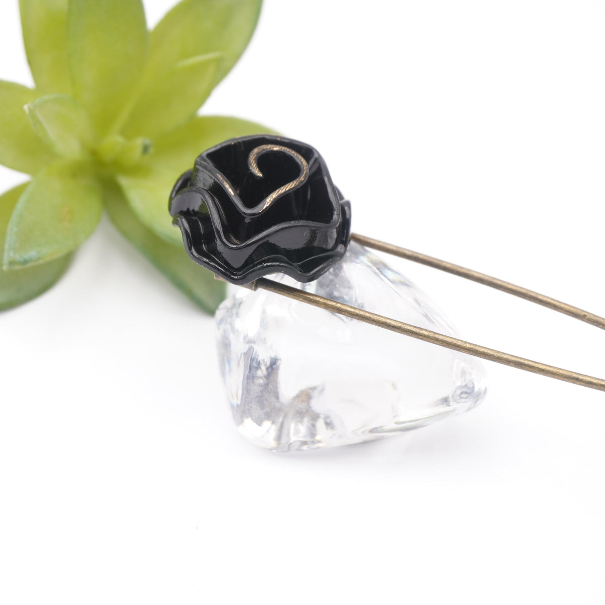 Schwarze Rose an bronzefarbener Nadel auf hellem Grund
