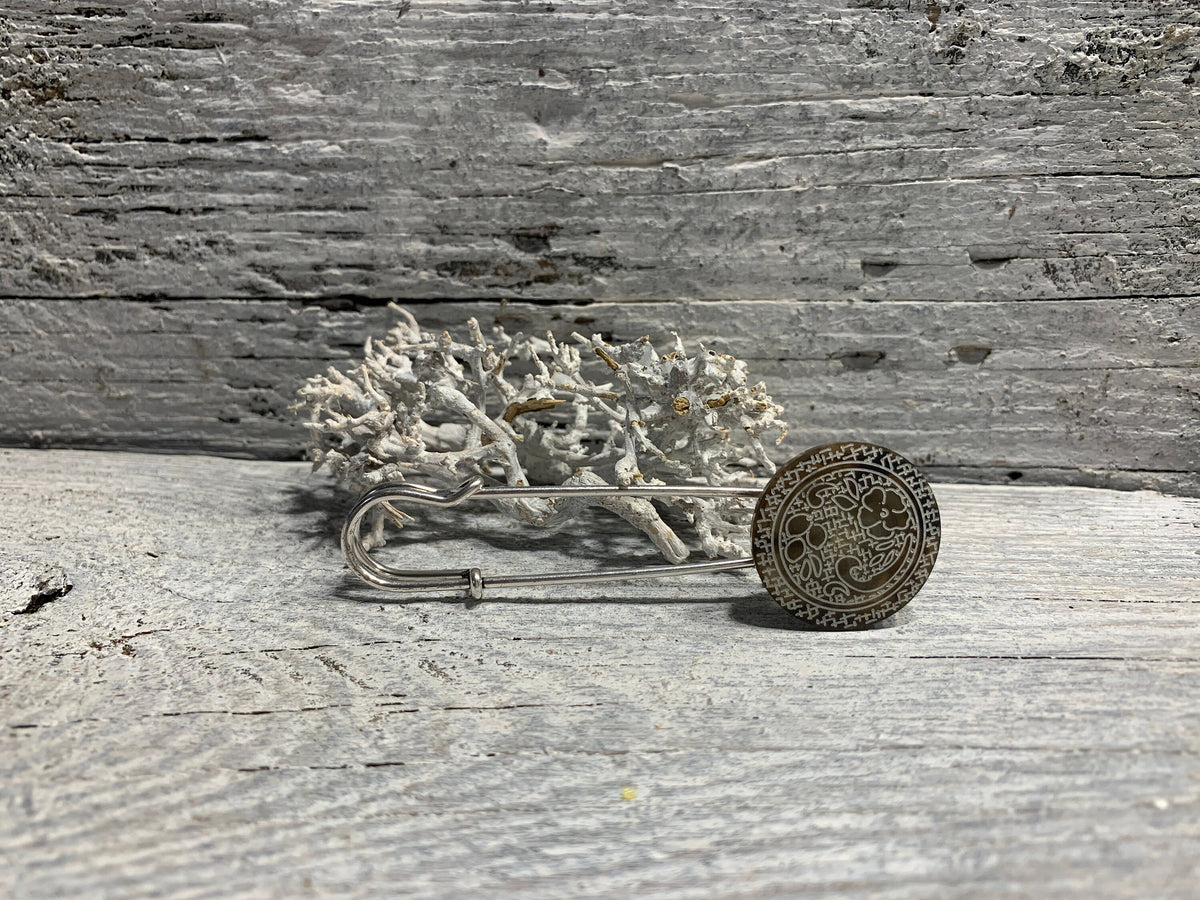 Ponchonadel mit Blumenornament in Taupe-Silberoptik auf verwittertem Holz vor Trockenflechte