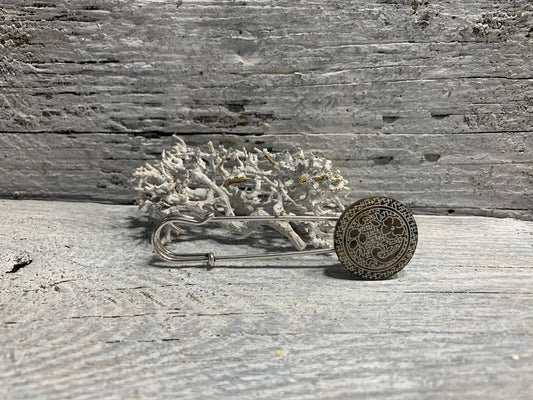 Ponchonadel mit Blumenornament in Taupe-Silberoptik auf verwittertem Holz vor Trockenflechte